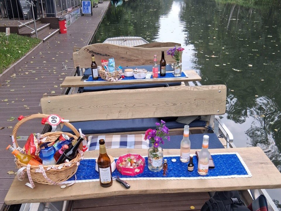 Picknickkorb mit einer 60, Getränke und Blumen auf dem Tisch eines Kahns, gedeckt für eine Geburtstagsfahrt