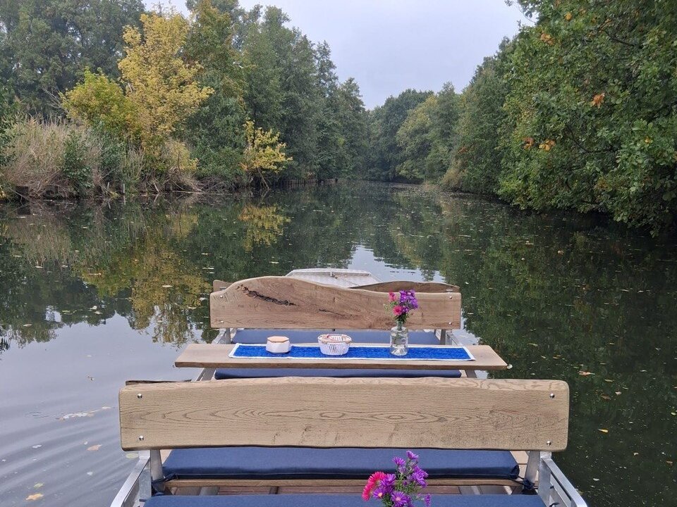 Kahn mit gedeckten Tischen und Blumen auf einem stillen, von herbstlichen Bäumen gesäumten Fließ